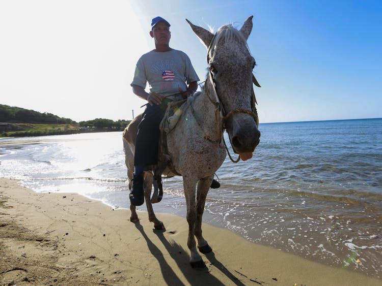 Man In Gray Shirt Riding A Horse On Beach