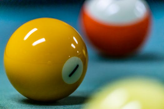Vibrant close-up of yellow billiard ball with blurred pool table background, emphasizing color and shape.