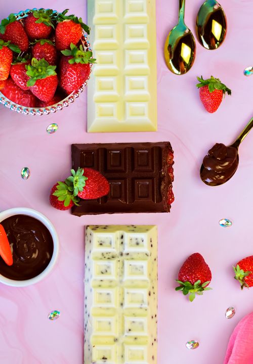 Free Delicious strawberries with dark, white, and milk chocolate bars on a pink surface. Stock Photo