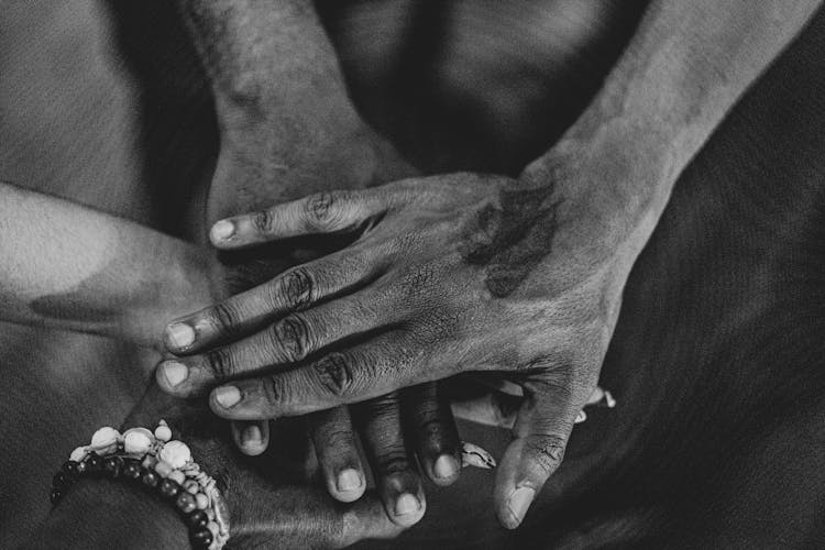 Grayscale Photo Of People's Hands Stacked Together