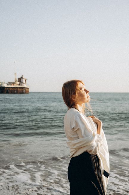 A serene moment captured of a woman standing by the sea with eyes closed, embracing sunlight and tranquility.