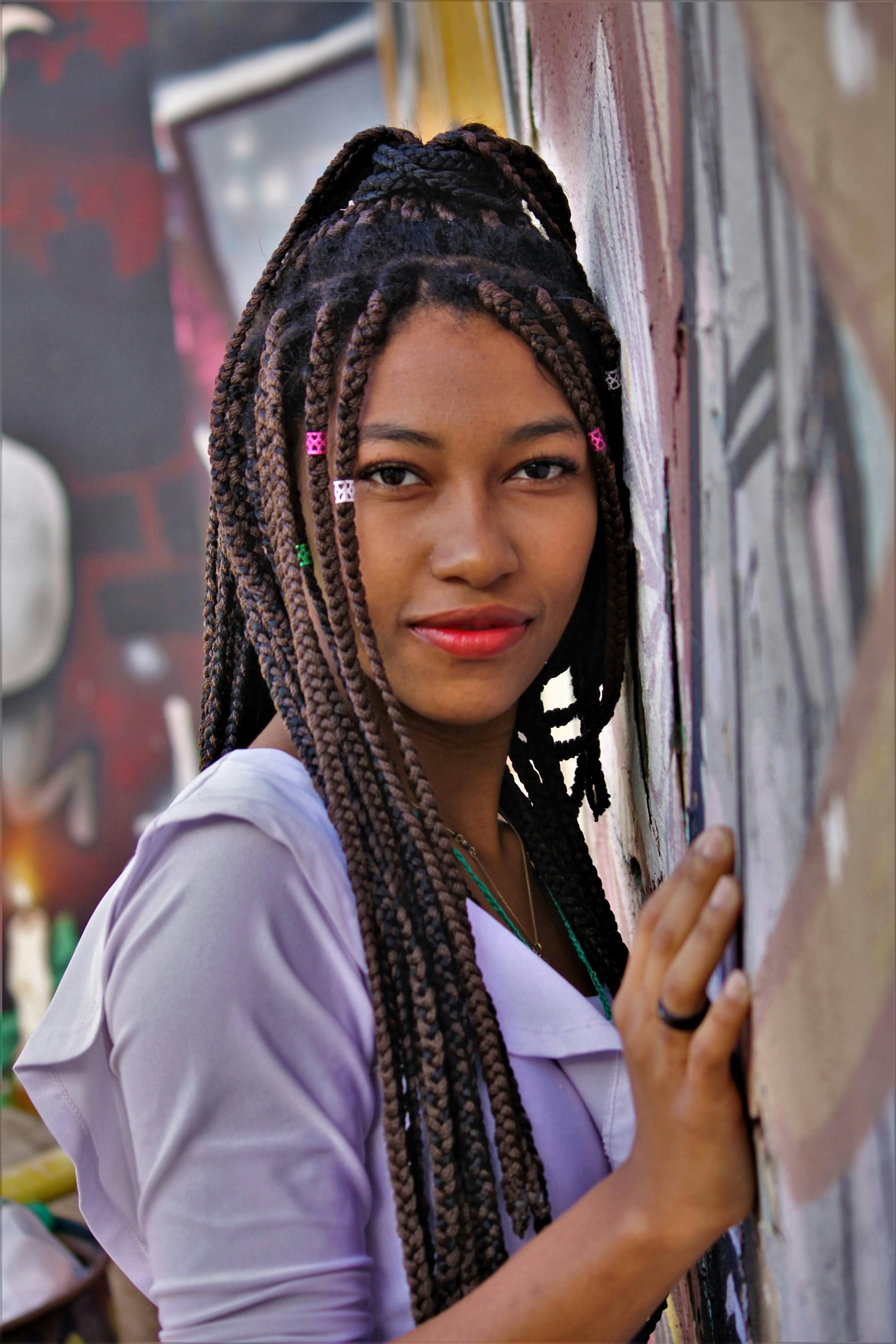 Close-up of a woman with braided hair leaning against a colorful wall.