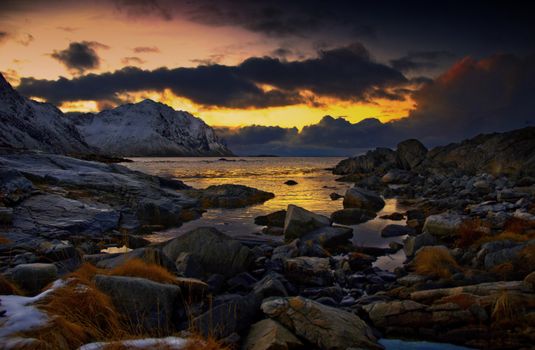 Breathtaking view of Nordland's rugged coast with snowy mountains and vibrant sunset hues.