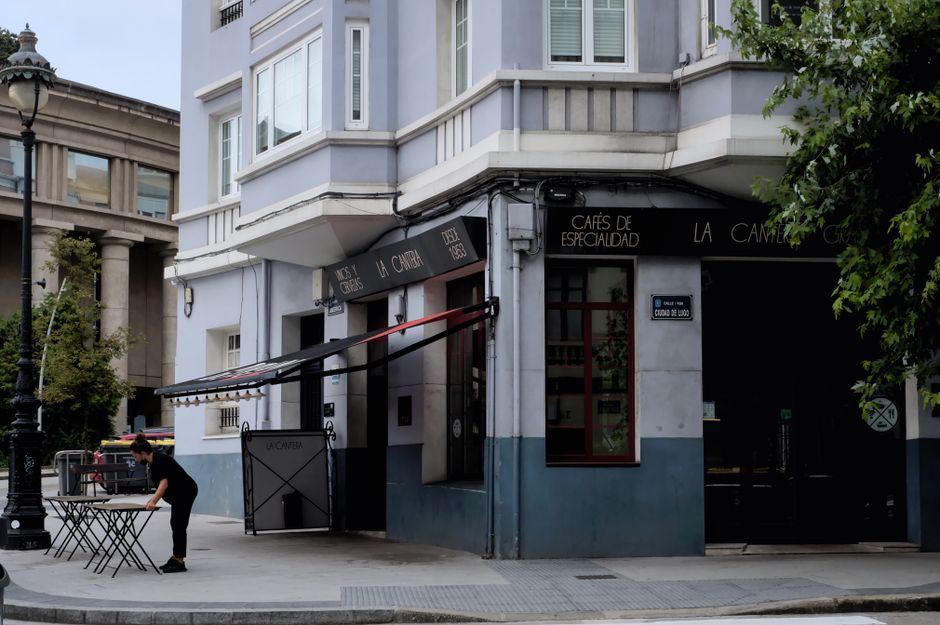 Vista de la calle de un café en A Coruña, mostrando la vida urbana con una camarera colocando mesas.