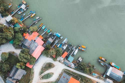 Free Vibrant aerial view showing docked boats and colorful buildings by a tranquil green river. Stock Photo