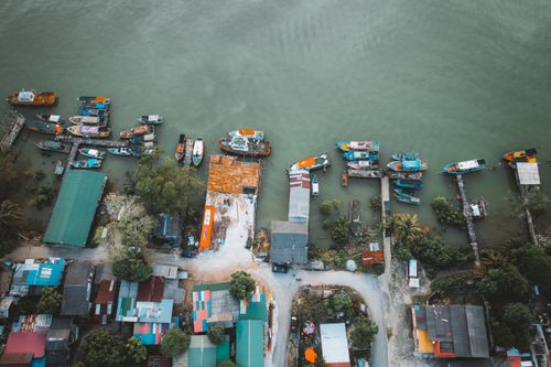 Free Drone capture of a vibrant coastal village with boats docked along the river. Stock Photo