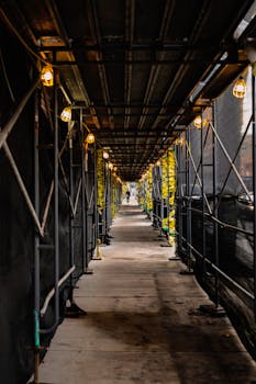 A lit passageway under a scaffolding on a city sidewalk, creating a dramatic depth effect.
