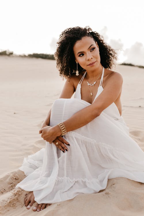 Pretty Woman Sitting on Beach in White Summer Dress