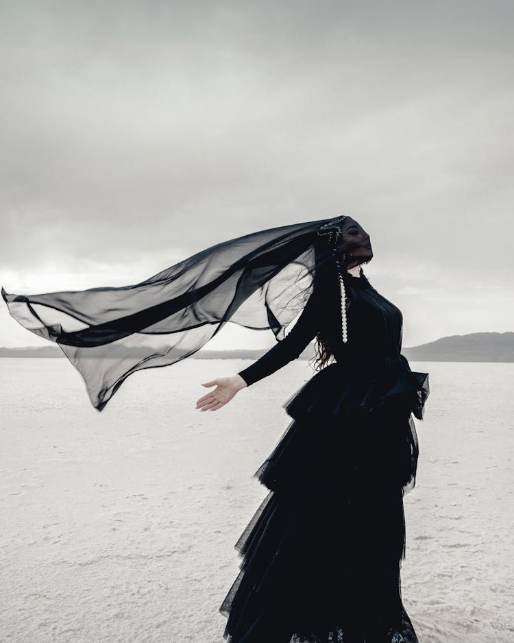 Woman In Black Veil Standing With Outstretched Arms In Desert