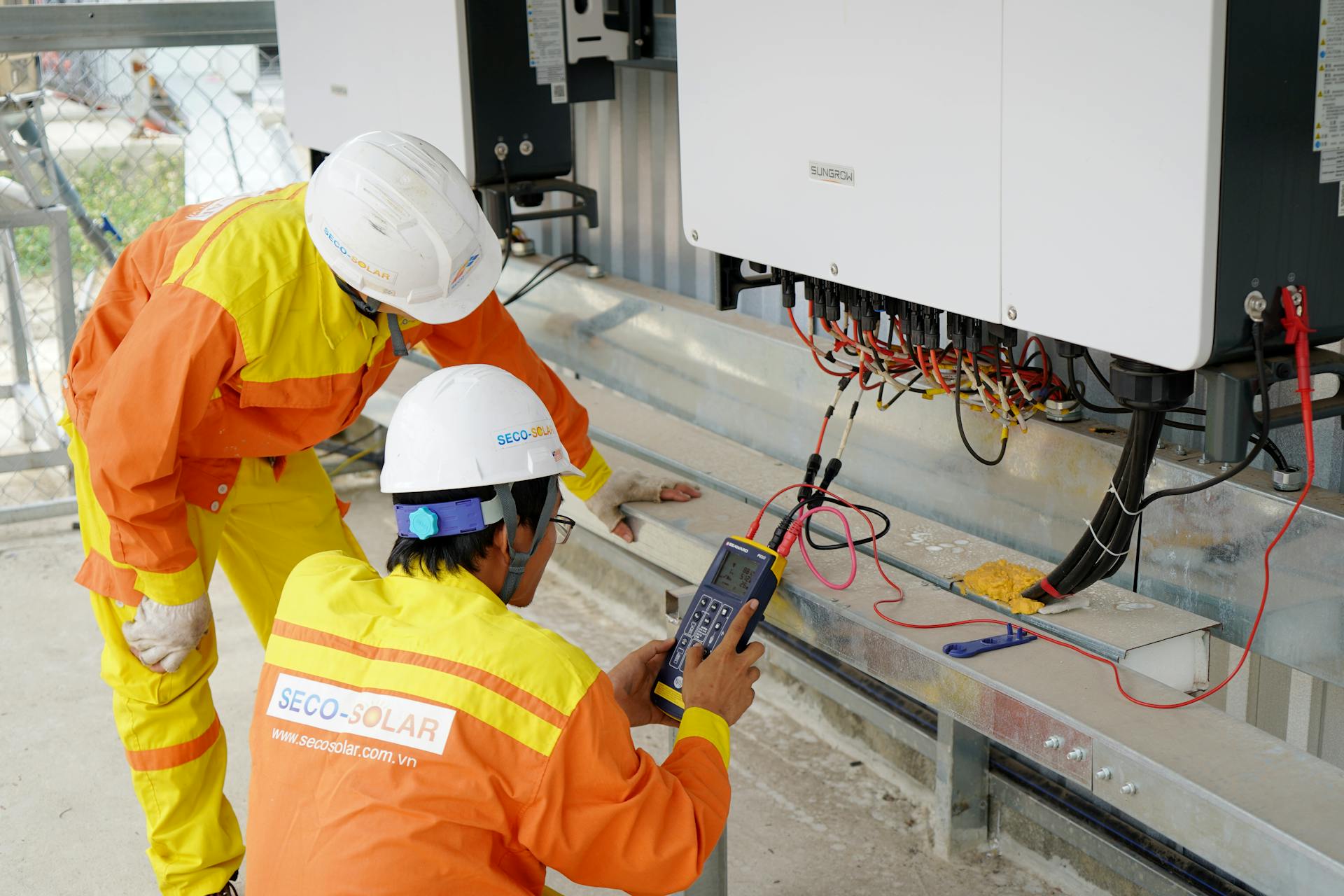 Two electrical engineers installing and testing solar power systems wearing safety gear at a construction site.