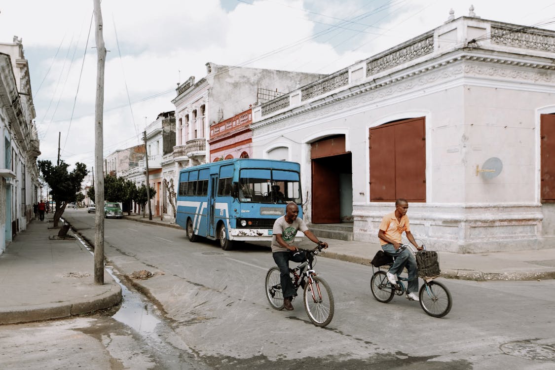 Free Man in Black Jacket Riding Bicycle Near Blue Bus Stock Photo