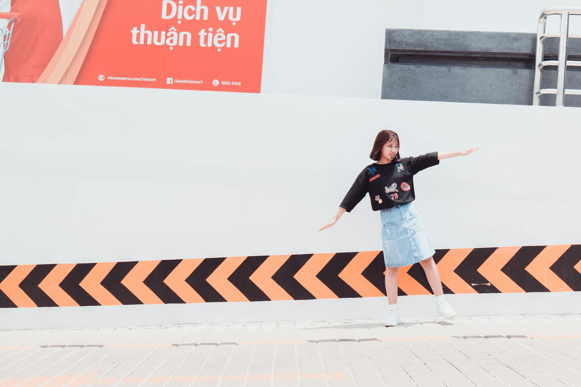 Asian woman posing in front of a modern sign outdoors, expressing joy and creativity.