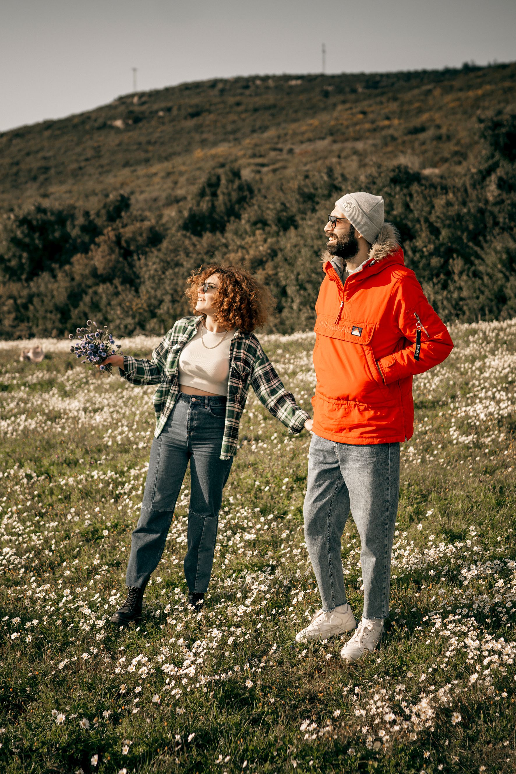 A joyful couple holding hands and walking through a sunny, flower-filled field.