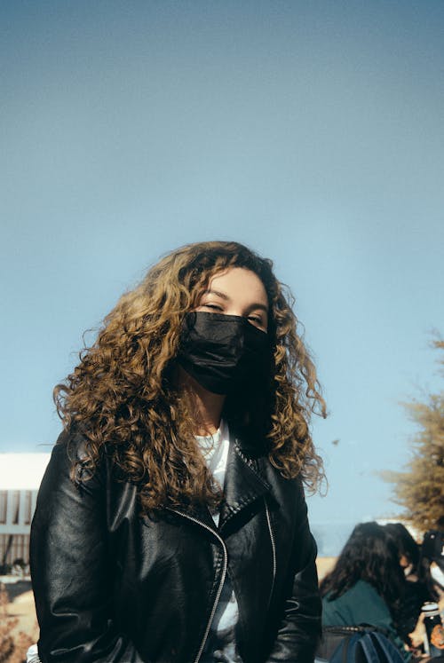 Woman in Black Leather Jacket Wearing Face Mask while Looking at the Camera