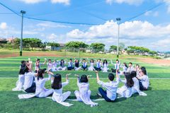 A large group of young people sitting in a circle, engaging in an outdoor activity on a sunny day.
