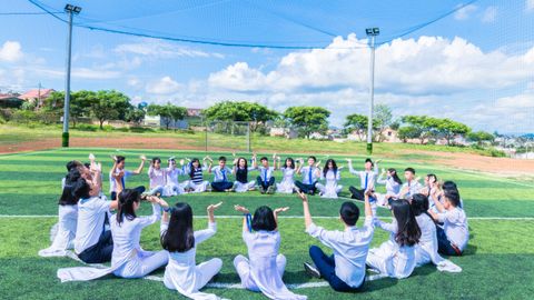 A large group of young people sitting in a circle, engaging in an outdoor activity on a sunny day.