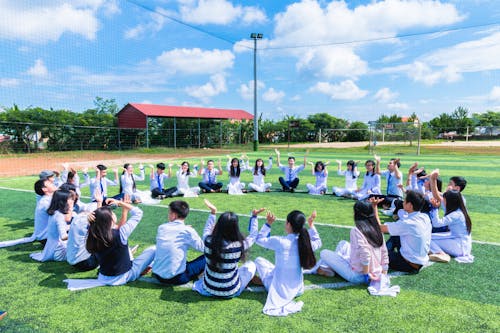 People Sitting on Green Lawn Grass While Doing Hands Up at Daytime