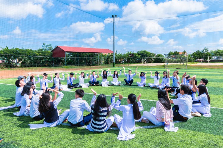 People Sitting On Green Lawn Grass While Doing Hands Up At Daytime