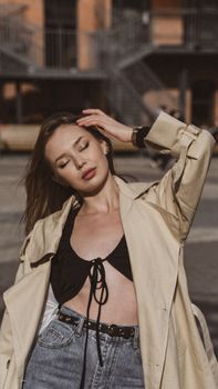 Confident woman in fashionable outfit with eyes closed, enjoying a sunny day in the city.