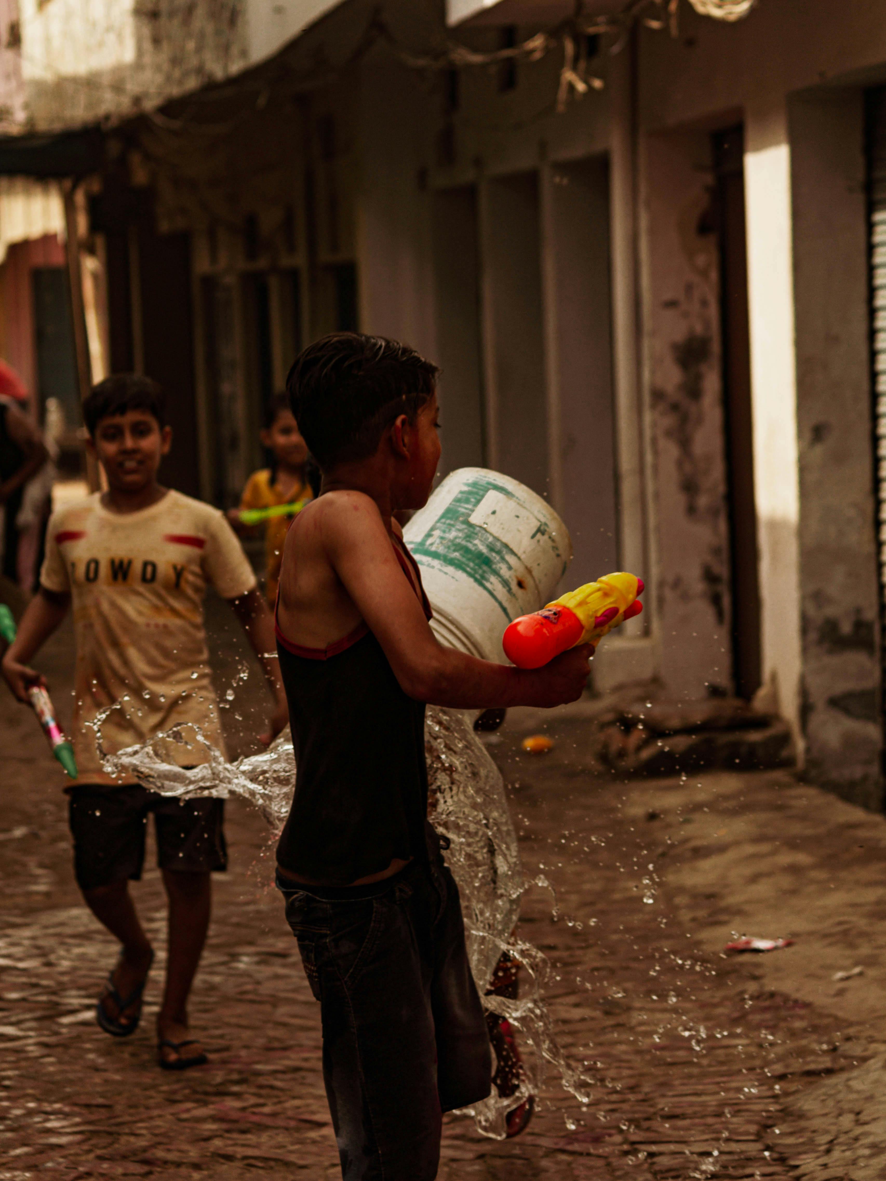 Boys enjoying a fun water fight with toys on a cobblestone street.