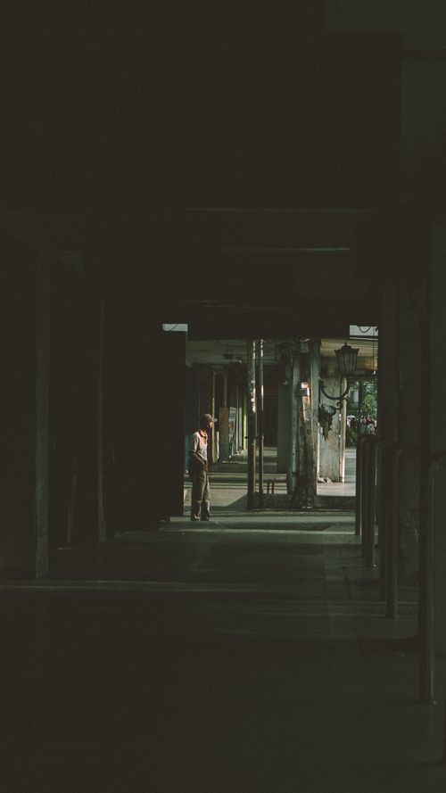 Free A lone figure stands in a shadowy Jogja alley, creating a contemplative silhouette at twilight. Stock Photo