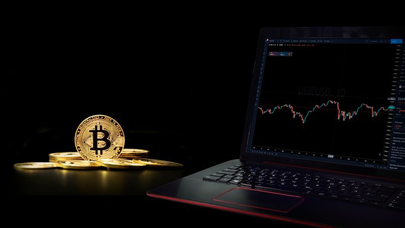 Golden bitcoin coins next to a laptop displaying a trading graph, symbolizing digital currency investment.