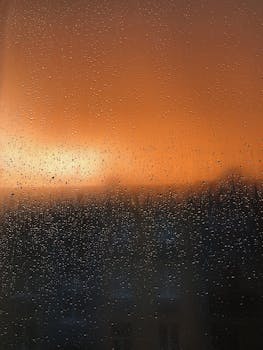 Captivating view of an orange sunset through a rain-speckled window, creating a peaceful ambiance.