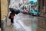 Woman walking on a rainy street with vintage cars, holding an umbrella, capturing urban weather scene.