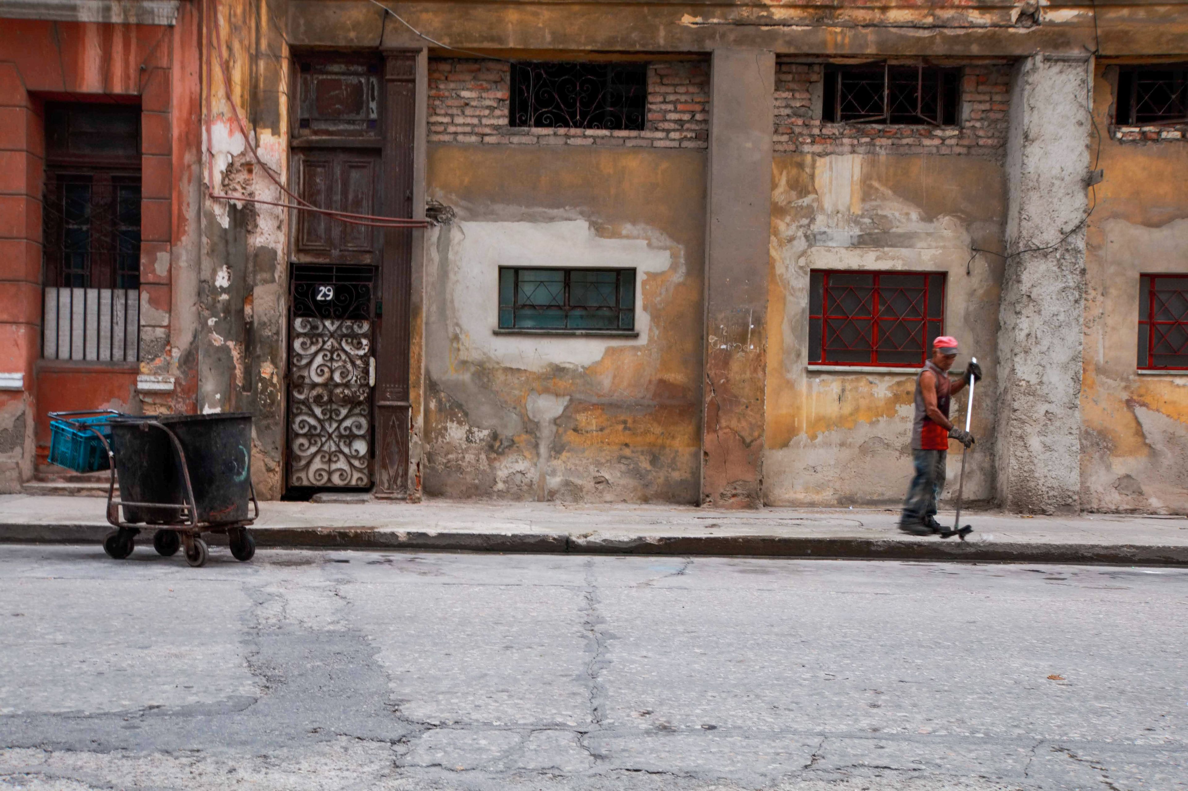 Man cleaning on a Cuban street with a rustic, worn backdrop. Captured in daylight.