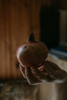 A close-up of a hand holding a fresh pomegranate indoors with warm lighting.