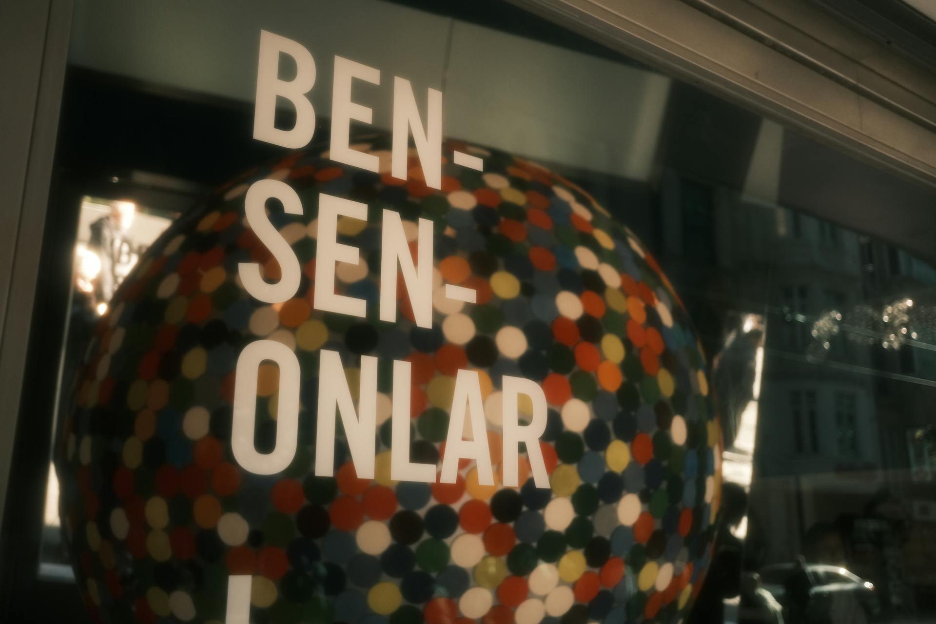 Abstract reflection of colorful dots on a glass sphere with text overlay in an urban setting.