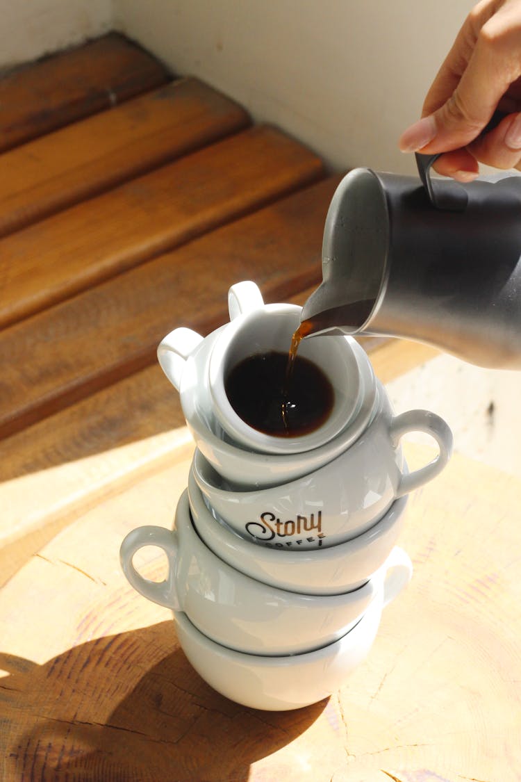 
A Person Pouring Coffee On A Stack Of Cups