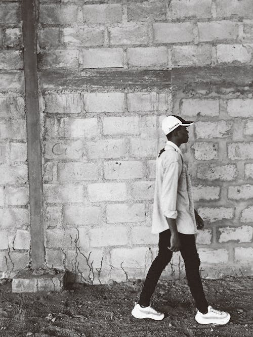 
A Grayscale of a Man Wearing a Cap Walking