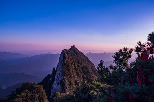 A breathtaking mountain peak surrounded by lush greenery and a vivid sunset sky.