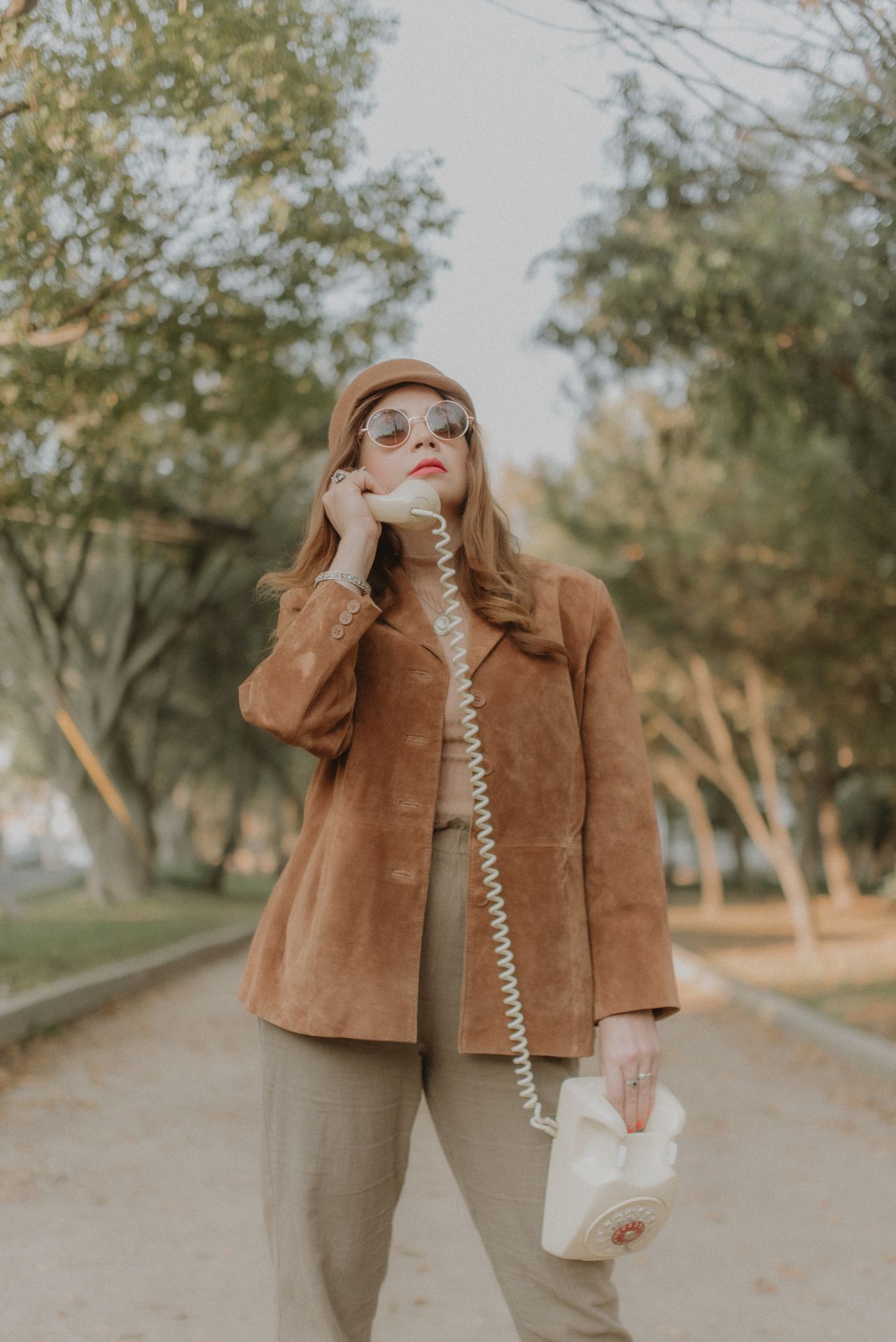 Woman in a tan suede jacket holding a vintage telephone outdoors