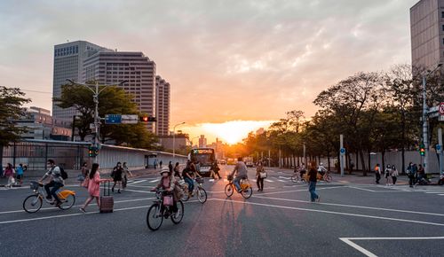 Free A vibrant urban scene with cyclists and pedestrians crossing a street in Taipei at sunset. Stock Photo