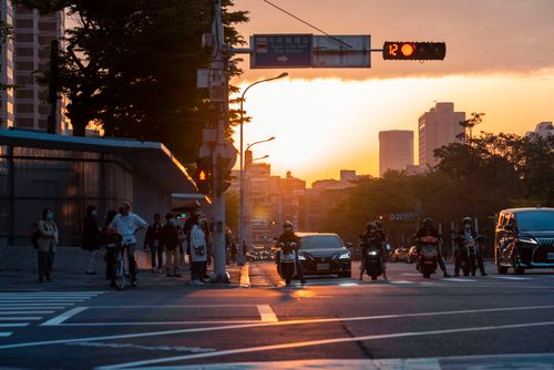 Free A bustling city street at sunset with cars, motorbikes, and people, capturing urban life. Stock Photo