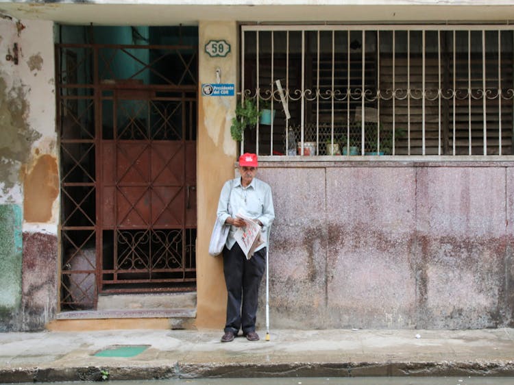 An Elderly Man Selling Newspapers Standing Outside A House