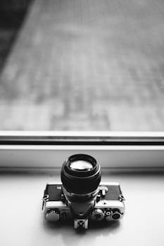 Black and white photo of a retro camera on a windowsill, showcasing classic design.