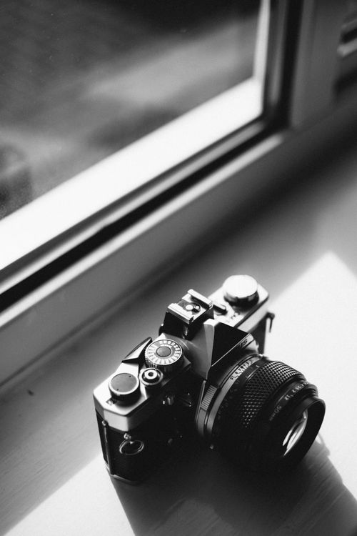 Free A classic vintage camera resting on a window sill, captured in black and white, showcasing retro photography equipment. Stock Photo