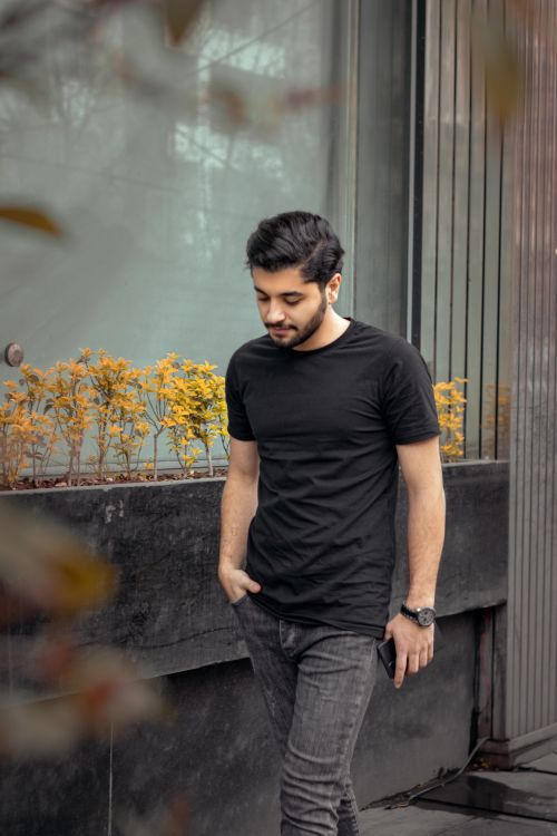 Free Casual fashion portrait of a young man walking by a modern building, wearing a black shirt and jeans. Stock Photo