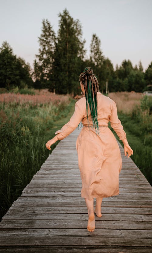 Woman in Brown Dress Walking on Wooden Pathway