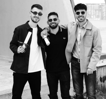 Three friends in sunglasses posing and smiling while holding diplomas outdoors.
