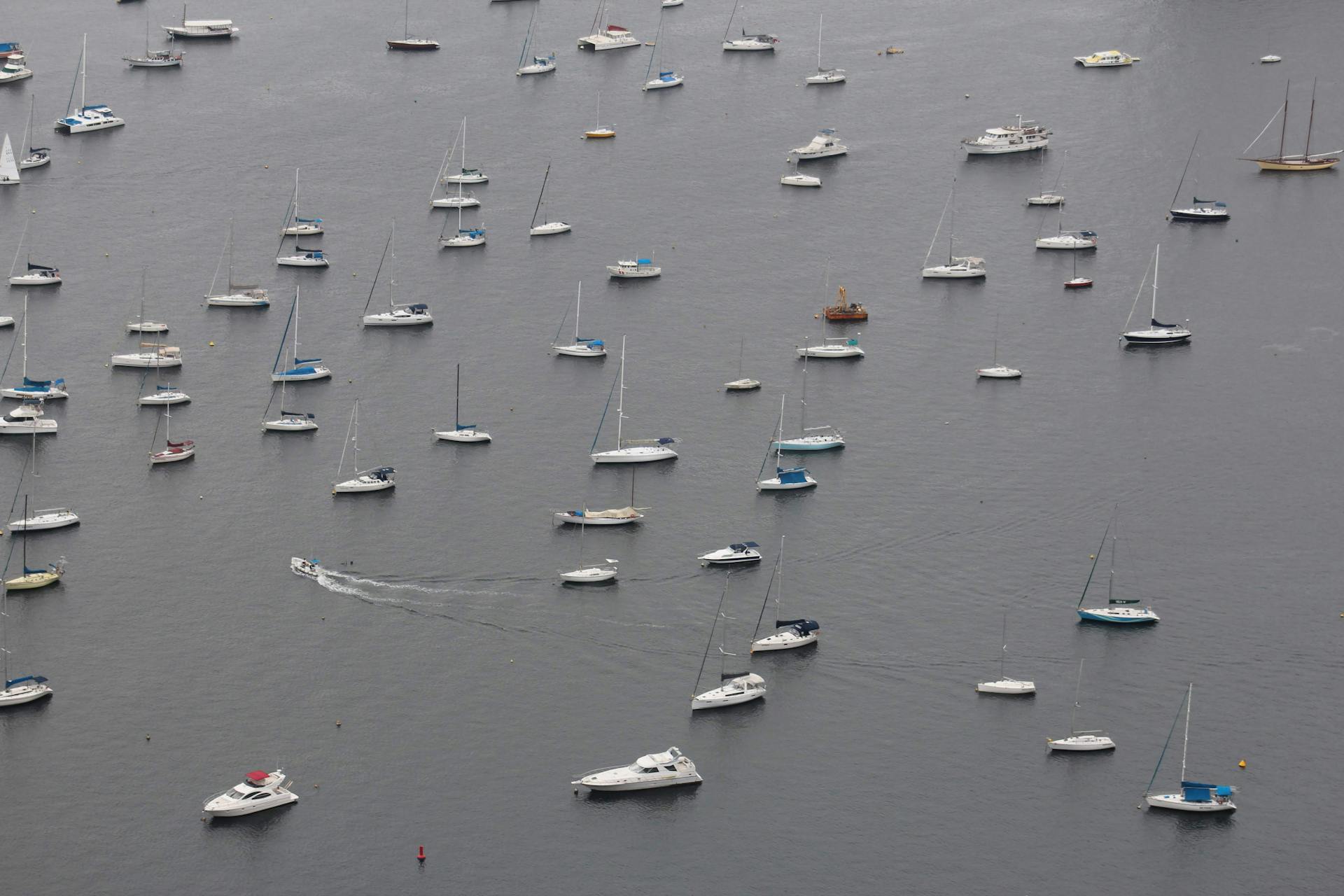 An aerial shot of numerous boats peacefully anchored in a large harbor under overcast skies.