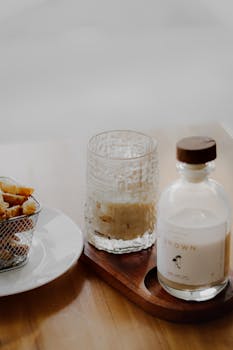 Elegant still life composition featuring a glass and beverage bottle on a wooden tray, perfect for dining themes.