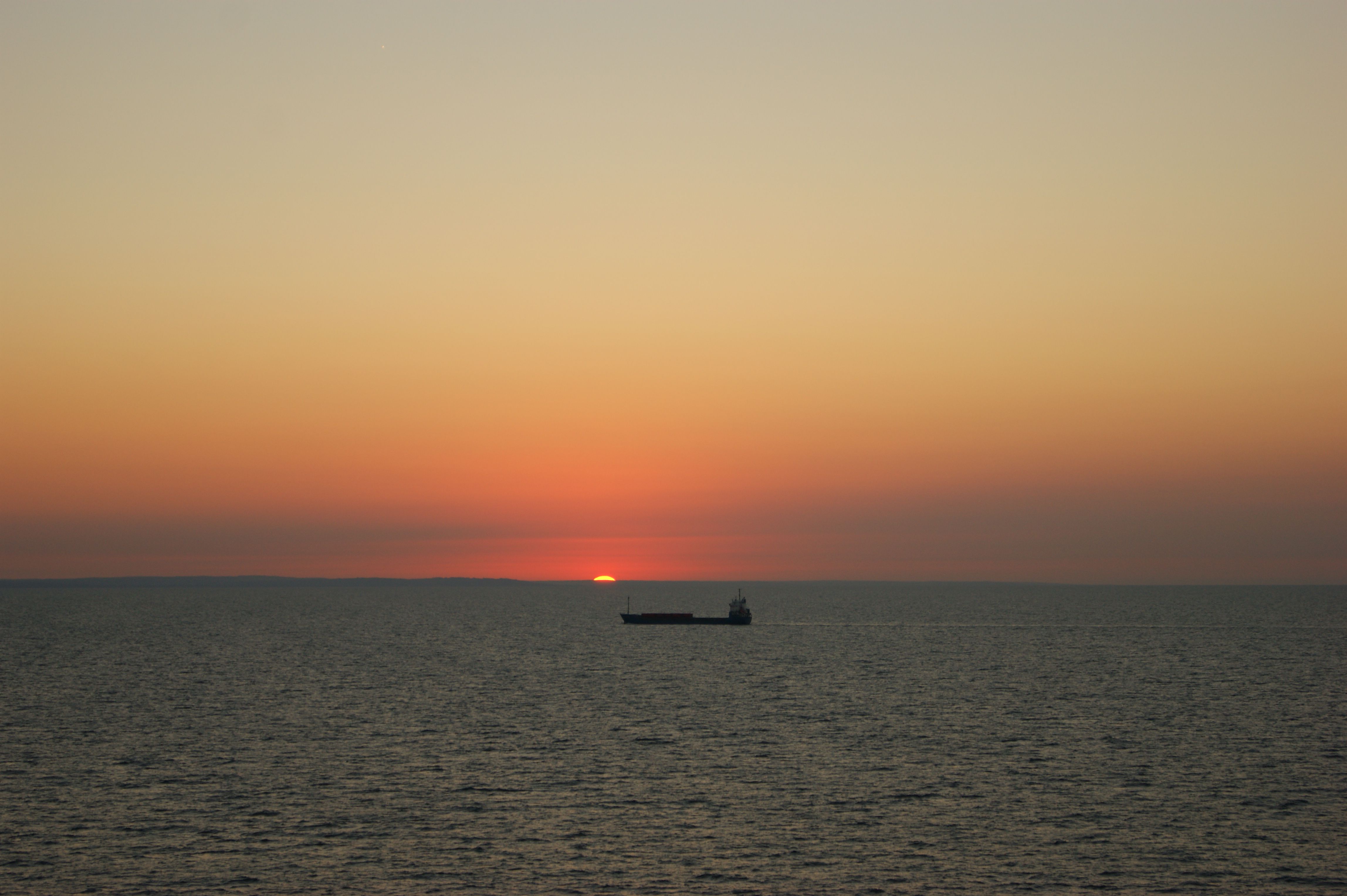 Tranquil view of a cargo ship against a vibrant ocean sunset, ideal for serene maritime themes.