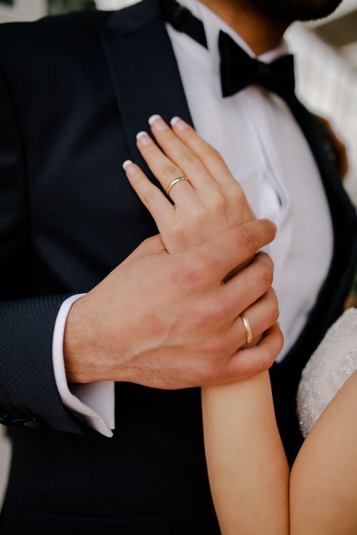 Free Close-up of a newlywed couple holding hands, showcasing wedding rings and a tuxedo. Stock Photo