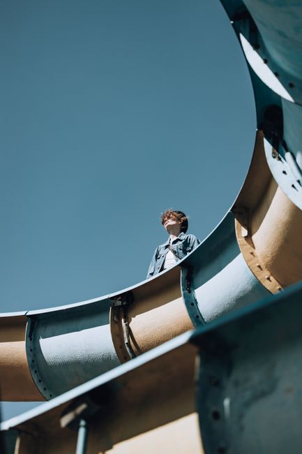 A man stands inside a large curved waterslide looking upwards against a blue sky.
