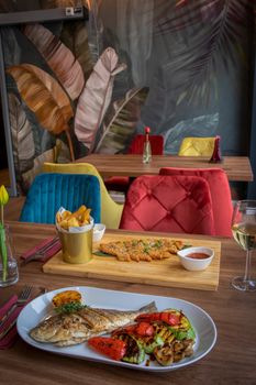 Gourmet meal featuring grilled fish and fries in a vibrant café interior with colorful decor and patterned walls.