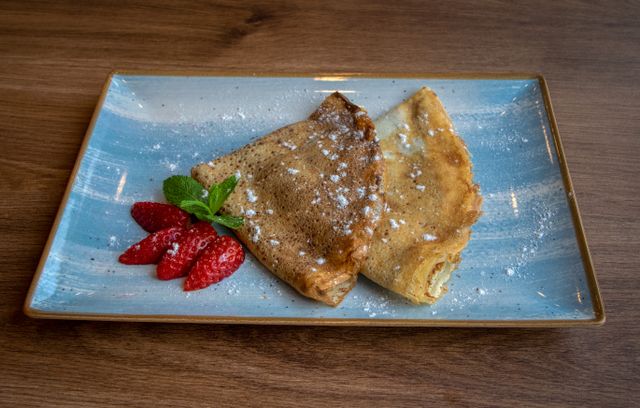 A plate of crêpes dusted with powdered sugar, served with strawberries and mint.